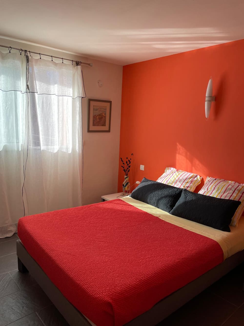 La chambre orange, son mur vermillon, sa fenêtre sur le jardin et son grand lit double